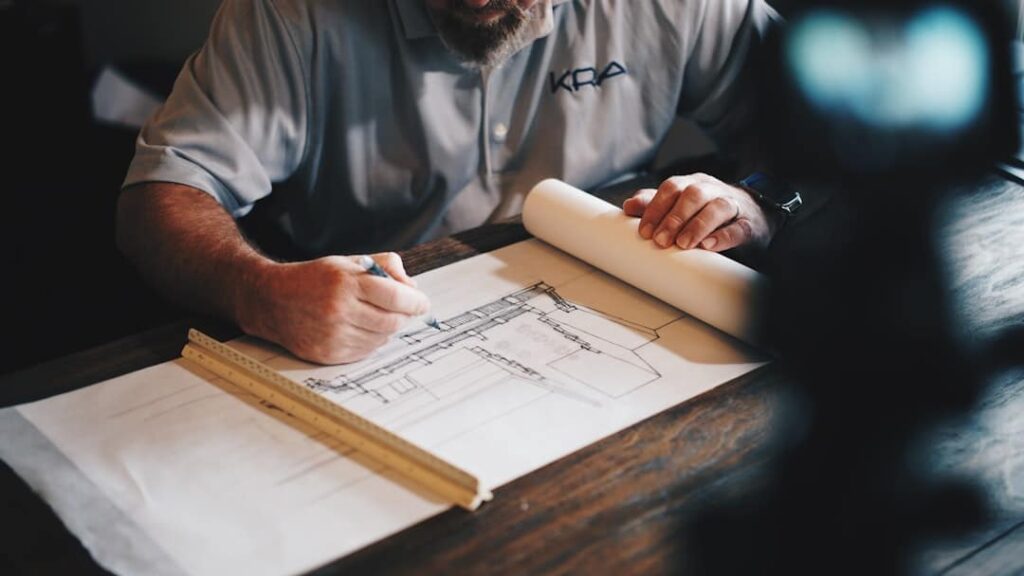 An architect drawing building plans on a large sheet of paper using a ruler.