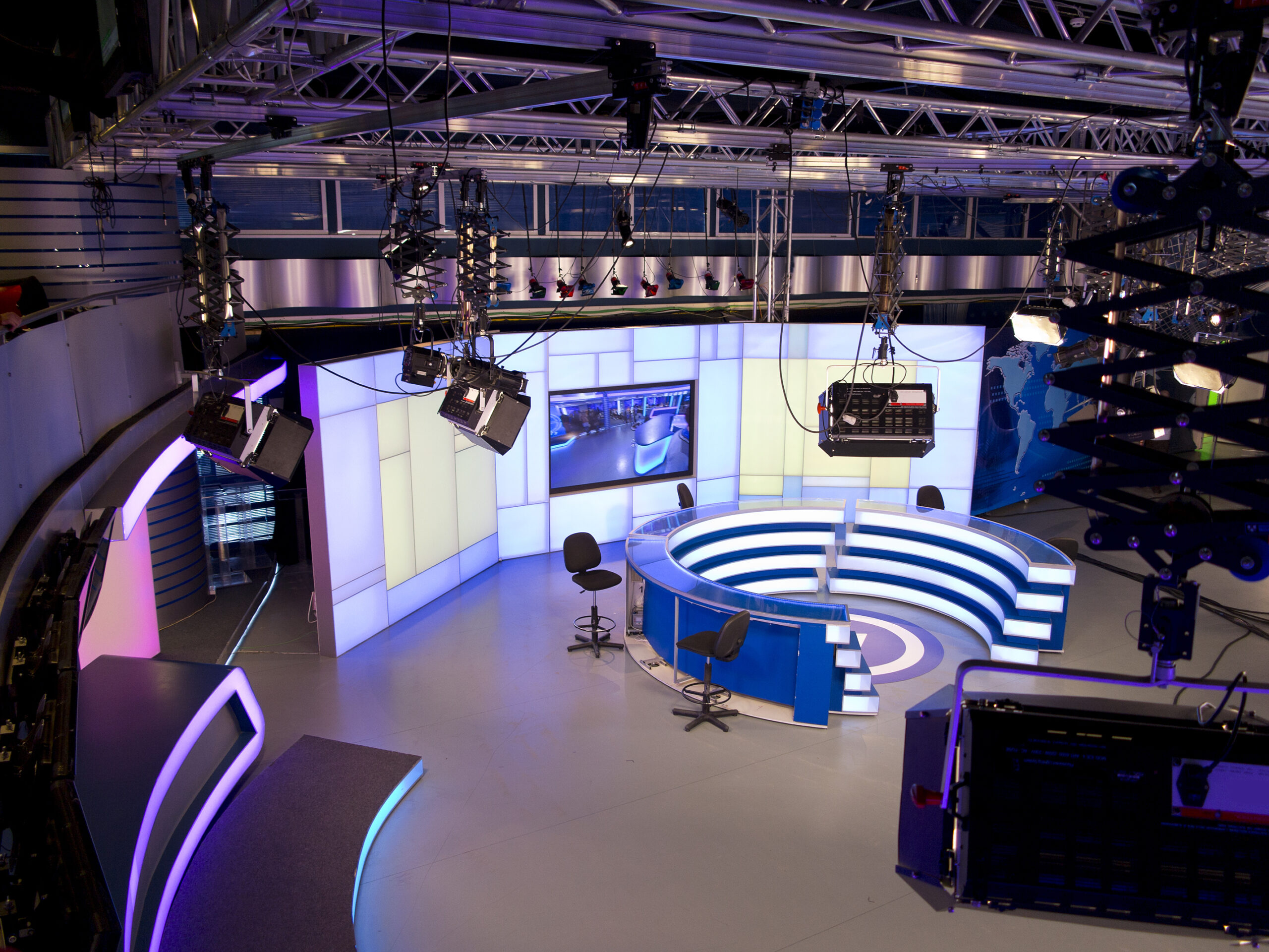 A high-tech TV news studio with circular LED-lit desks and ceiling-mounted lights.